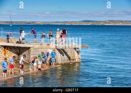 Un groupe de vacanciers avec la pêche aux crabes des nids sur le mur du port à St Ives, Cornwall, UK Banque D'Images