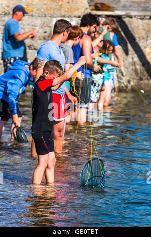 Un groupe de vacanciers avec la pêche aux crabes des nids sur le mur du port à St Ives en Cornouailles, Royaume-Uni Banque D'Images