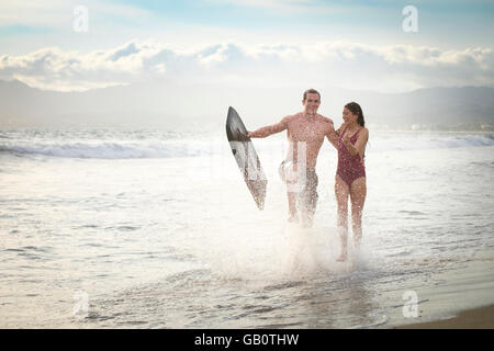 Jeune couple tourne à la plage avec boogie board, les projections d'eau. Riviera Nayarit, Mexique. Banque D'Images