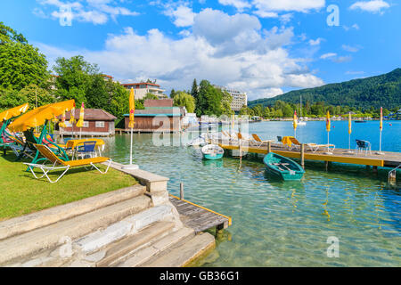 WORTHERSEE LAKE, AUTRICHE - JUN 20, 2015 : bateaux de touristes et de chaises longues avec parasols sur la jetée en bois de beau lac alpin Millepertuis Banque D'Images