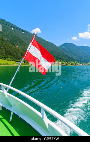 De brandir le drapeau de l'Autriche sur le vent pendant la croisière bateau sur l'eau verte du lac Weissensee, Autriche Banque D'Images