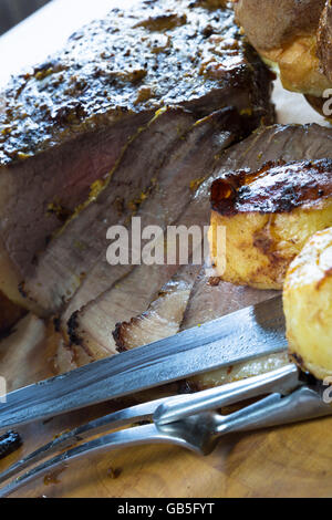 Un petit-déjeuner anglais fraîchement rôti de boeuf partiellement sculptés sur une planche en bois avec quelques pommes de terre, prêt à servir. Banque D'Images