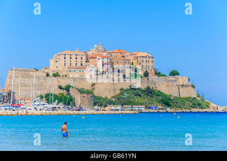 CALVI, CORSE - 28 juin 2015 : dans l'eau de mer et la vue de la citadelle avec maisons à Calvi port en arrière-plan, Cor Banque D'Images