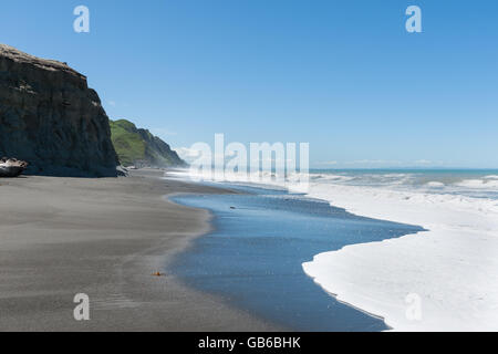 Les vagues déferlent sur South Pacific plage bordée de falaises en Nouvelle-Zélande menant mousse blanche laver comme ils retournent. Banque D'Images