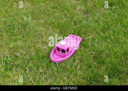 Un jouet d'enfant en plastique rose chaud plastique voile assise seule dans l'herbe verte Banque D'Images