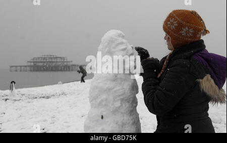 Une femme apporte la touche finale à son bonhomme de neige sur la plage de Brighton. Banque D'Images