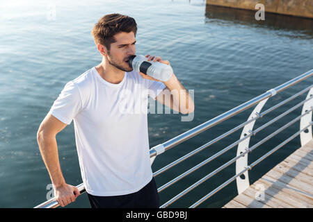 Young sportsman debout sur une terrasse en bois près de la mer et de l'eau potable Banque D'Images