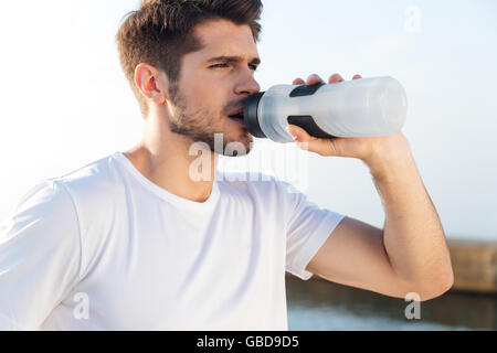 Gros plan du jeune sportif en chemise blanche à l'extérieur de l'eau potable Banque D'Images