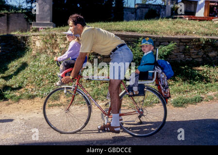 Un père fait du vélo avec deux enfants, les enfants sont assis dans un siège enfant Banque D'Images