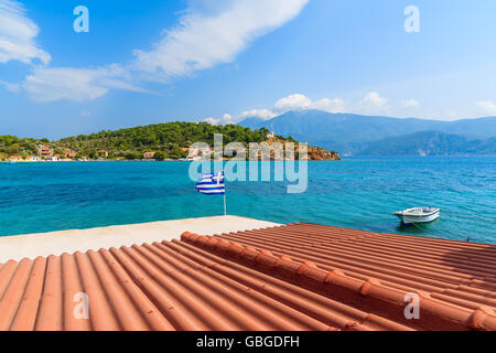 Tuile Orange toit d'une maison avec de brandir le drapeau grec contre l'arrière-plan de la mer bleue sur la côte de l'île de Samos, Grèce Banque D'Images