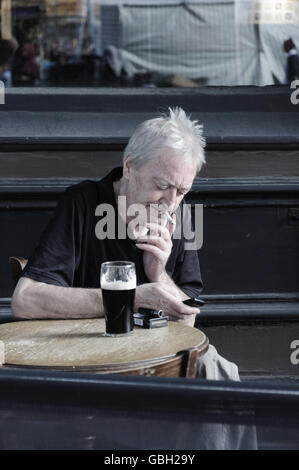 Londres - Angleterre. Un homme est contrôler son téléphone tout en buvant de la bière à l'extérieur d'un pub à Whitechapel. Banque D'Images