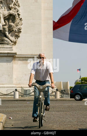 Le journal The Times Charles Bremner, correspondant monte un vélo Vélib' passé l'Arc de Triomphe Paris, France, 15 juillet 2007. Banque D'Images