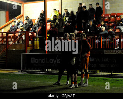 Les fans dans les stands regardent sur le terrain tandis que les joueurs se tiennent sur le terrain ci-dessous avant que le match de la Coca-Cola League 2 n'ait été abandonné en raison de problèmes de projecteurs à Victoria Road, Dagenham. Banque D'Images