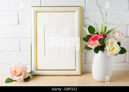 Maquette du châssis blanc sur mur de brique avec des roses. Cadre blanc vertical immersive pour portrait ou de l'affiche. Cadre blanc vide pour maquette de Banque D'Images