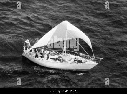 L'équipage gai d'un yacht de course Fastnet se déporte vers l'hélicoptère de contrôle alors qu'il est aperçu sous un banc de juré, à 150 miles au nord-ouest de St Ives, après que des galas féroces aient fait 15 morts. Banque D'Images