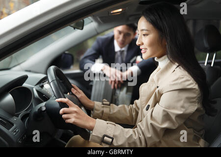 Le vendeur de voiture pour aider la jeune femme dans la voiture de route Banque D'Images