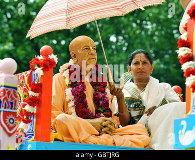 Un dévot de Hare Krishna garde le soleil sur une statue en bois sur un sanctuaire à roulettes décoratif géant, l'un des trois qui a été tiré à la main de Hyde Park à Trafalgar Square pour célébrer le festival « Ratha-yatra ». Banque D'Images