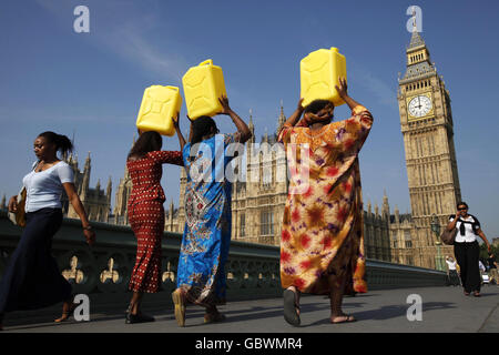 Une femme africaine et asiatique portant une robe traditionnelle porte des jerricans remplis d'eau de la Tamise à Downing Street à Londres, où elle va remettre 80,000 lettres du public britannique, au nom de la campagne End Water Poverty. Banque D'Images