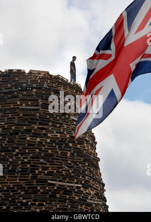 PHOTO AUTONOME Un homme se tient au sommet d'un feu de joie à NewtownabbabbabbabbabbabbabbabbabbabbabbaLes feux de joie seront mis à feu à travers l'Irlande du Nord le 11 juillet ou la onzième nuit avant les douzième célébrations. Banque D'Images