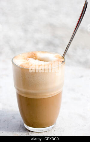 Un verre de caffè latte avec du sucre sur le dessus et une cuillère qui sort, assis sur une table de marbre Banque D'Images