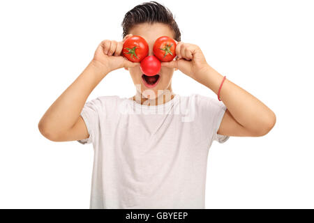 Enfant joyeux avec un nez de clown rouge tenant deux tomates devant ses yeux isolé sur fond blanc Banque D'Images