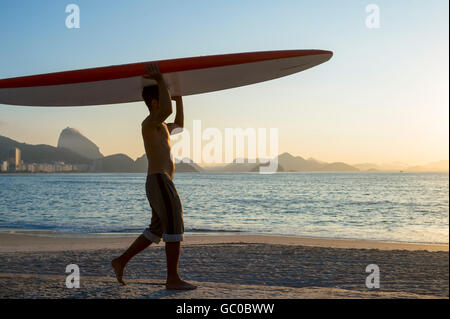 RIO DE JANEIRO - 5 avril, 2016 : un jeune homme brésilien sur la plage de Copacabana, équilibre un surf sur sa tête au lever du soleil. Banque D'Images