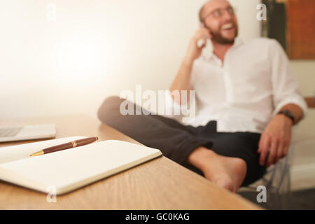 Sur 24 avec l'homme assis en arrière-plan en conversation sur téléphone mobile. Businessman working from home office. Banque D'Images