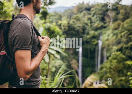 Close up shot of young man with backpack debout dans la nature et à la recherche à cascade. Male hiker près de cascade dans la forêt. Banque D'Images