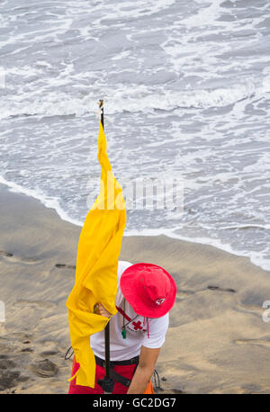 Croix Rouge lifeguard plaçant drapeau jaune sur la plage en Espagne Banque D'Images