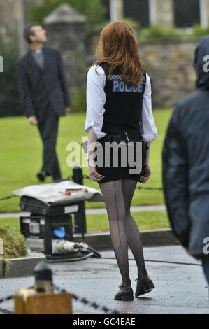 L'assistante du médecin, l'actrice Karen Gillan, habillée comme officier de police, tire sa jupe courte vers le bas pendant le tournage sur un terrain près de la cathédrale de Llandaff, Cardiff, pays de Galles, où la dernière série de Doctor Who est filmée. Banque D'Images