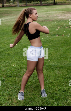 Jolie Fille de l'adolescence de race blanche faisant des exercices de torsion dans un short blanc et noir Haut Standing On Green Grass In Park Banque D'Images