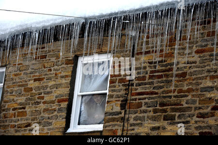 Une femme regarde par sa fenêtre à Allendale, dans le Northumberland, comme de grandes glaces pendent du toit après de fortes chutes de neige. Banque D'Images