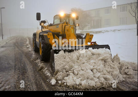 Un excaveur JCB élimine la neige à Princetown, Dartmoor, Devon, où la neige est tombée la nuit et s'est bloquée au large de la ville. Banque D'Images