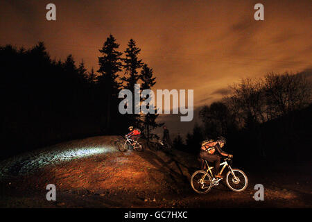 L'un des nombreux motards de montagne part pour une promenade nocturne humide avec seulement une torche pour éclairer leur chemin sur de fortes collines au-dessus des rochers et à travers les bois sur l'un des sentiers de VTT les plus populaires d'Écosse Glentress, dans les frontières écossaises. Banque D'Images