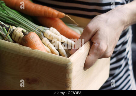 Close up of awoman tenant une grande caisse en bois plein de matières, des légumes fraîchement récoltés. Banque D'Images