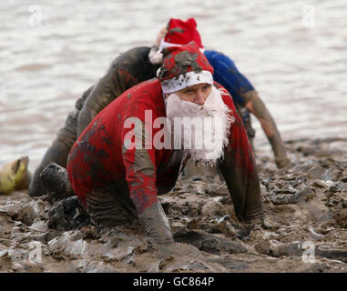 Un concurrent portant une tenue du Père Noël rampant sur la rive vers la ligne d'arrivée à la fin de la course de Maldon Mud à Maldon, dans l'Essex. Banque D'Images