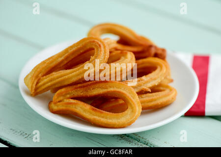 Libre de quelques churros typiques de l'Espagne sur une plaque en céramique blanc, placé sur une table en bois rustique bleu pâle Banque D'Images