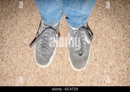 Close up de la partie inférieure des jambes et des pieds de la personne portant des jeans en denim bleu et gris Converse formateurs Banque D'Images