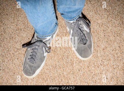 Close up de la partie inférieure des jambes et des pieds de la personne portant des jeans en denim bleu et gris Converse formateurs Banque D'Images