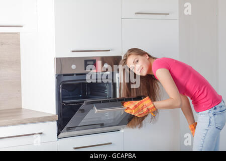 Belle jeune femme la cuisine dans une cuisine moderne. une fille prépare des aliments dans le four. Banque D'Images