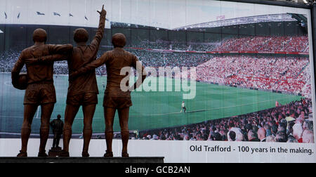 Une affiche à l'extérieur du stade Old Trafford de Manchester United célébrant les 100 ans du stade Old trafford est également représentée sur la photo : la statue de Denis Law, Sir Bobby Charlton et George Best et la statue de Sir Matt Busby (arrière-plan) Banque D'Images