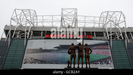 Une affiche à l'extérieur du stade Old Trafford de Manchester United célébrant les 100 ans du stade Old trafford est également représentée sur la photo : la statue de Denis Law, Sir Bobby Charlton et George Best et la statue de Sir Matt Busby (arrière-plan central) Banque D'Images