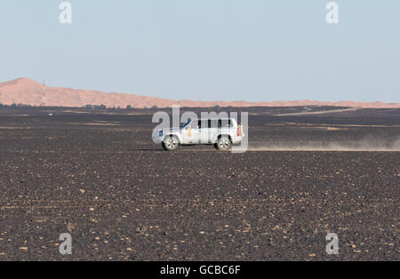 Range Rover argent voyageant à Stony Maroc désert, la position droite à gauche, le ciel bleu et les montagnes en arrière-plan. Banque D'Images