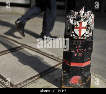 Un travailleur passe devant un bollard portant les armoiries de la City of London Corporation, dans le Square Mile de Londres. Banque D'Images