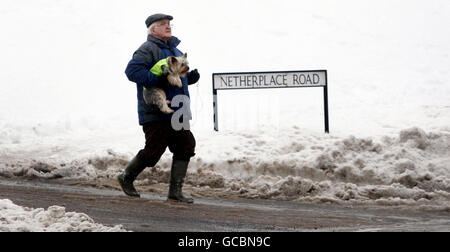 Un homme marche sur une route à Newton Mearns après une lourde chute de neige à travers l'Écosse pendant la nuit. Banque D'Images