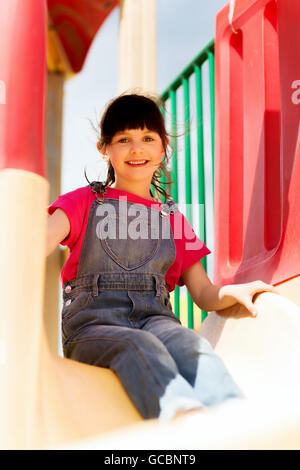 Happy little girl sur la diapositive à l'aire de jeux pour enfants Banque D'Images