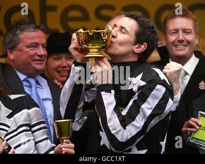 Le jockey Paddy Brennan embrasse la coupe d'or Cheltenham après que le commandant impérial remporte la coupe d'or Totesport Cheltenham alors que l'entraîneur Nigel Twiston-Davies (à gauche) regarde Banque D'Images