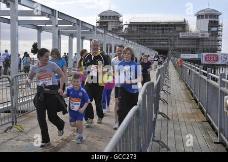 Des coureurs de charité courent le long de Weston-super-Mare Grand Pier alors qu'ils participent à la course de charité de Sainsbury's Sport relief Mile. Banque D'Images