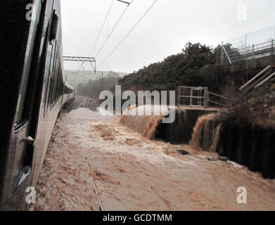L'eau d'une rivière aux frontières qui a fait éclater ses inondations de rive sur la ligne principale de la côte est au nord de Berwick, entraînant un ralentissement des trains à un rythme de marche. Banque D'Images