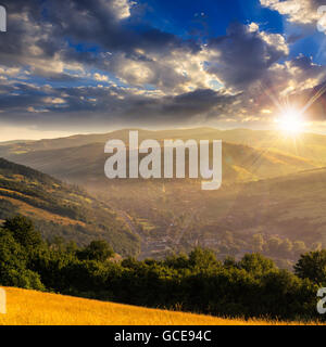 Paysage d'été. Village sur le flanc de la montagne avec la forêt dans le brouillard au coucher du soleil Banque D'Images